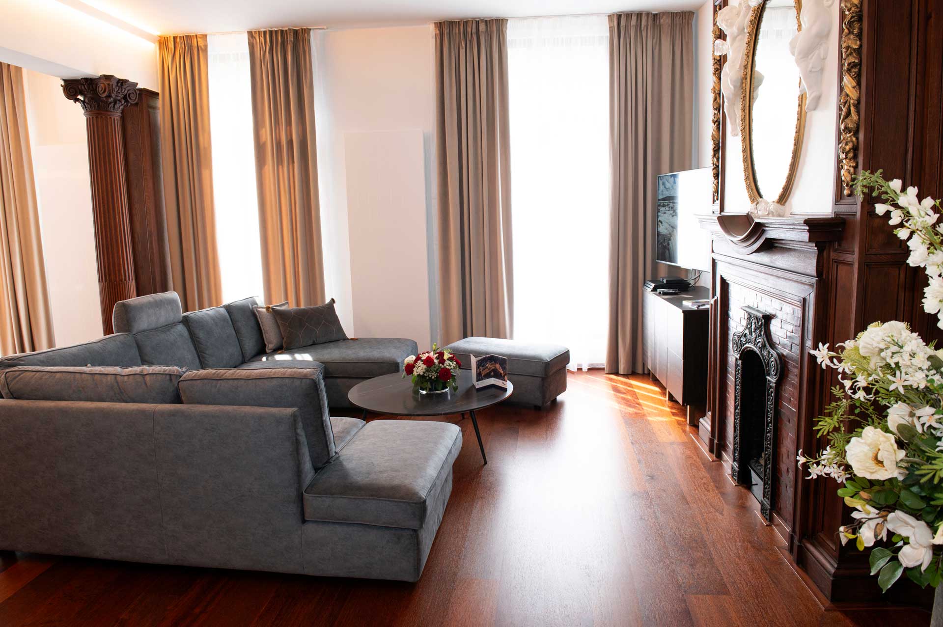 living room with grey corner sofa and wooden columns – Suite Rubens, Botanique Suites Antwerp